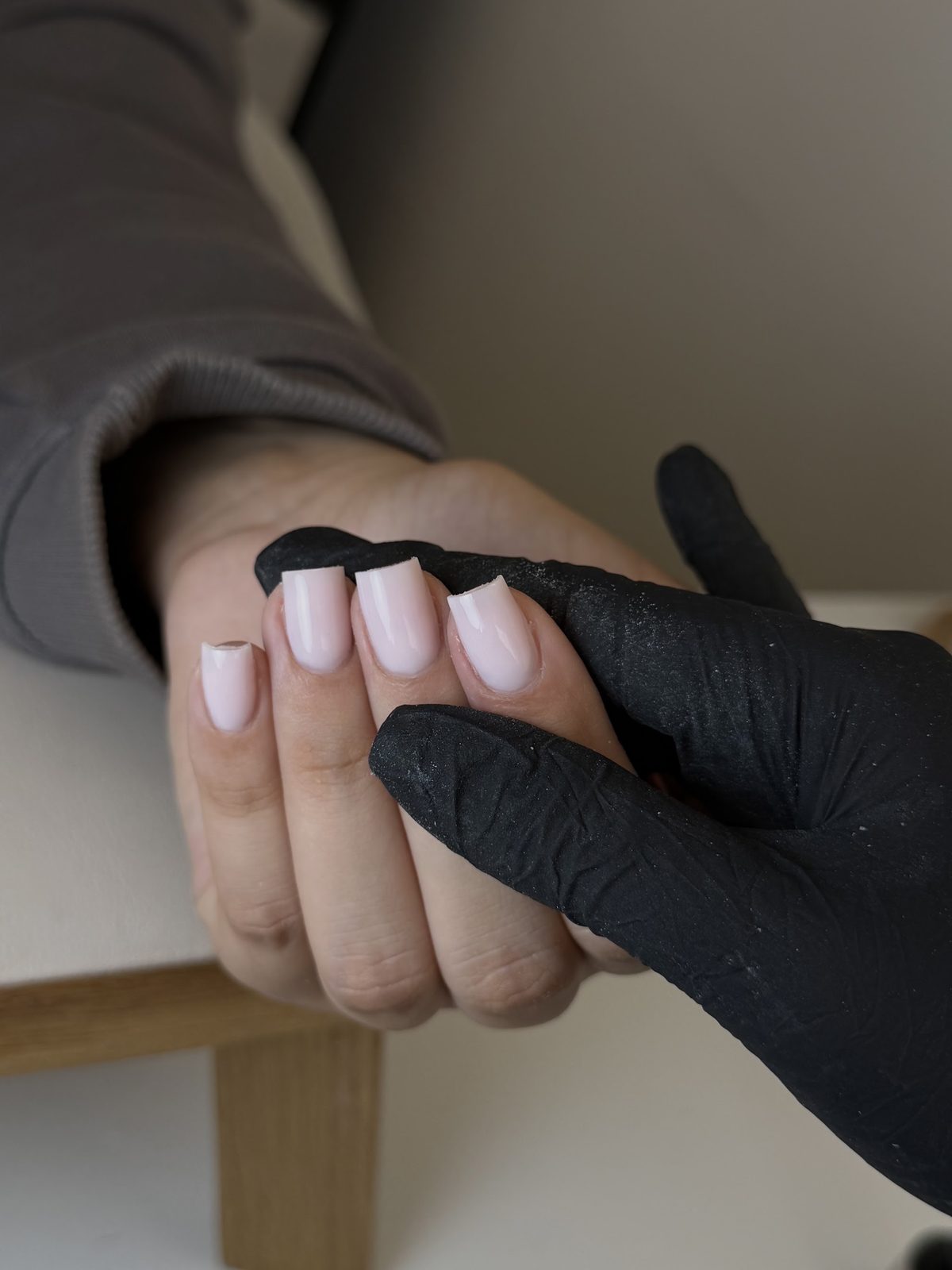 Een hand met lichtroze vierkante nagels rust in een hand met een zwarte handschoen