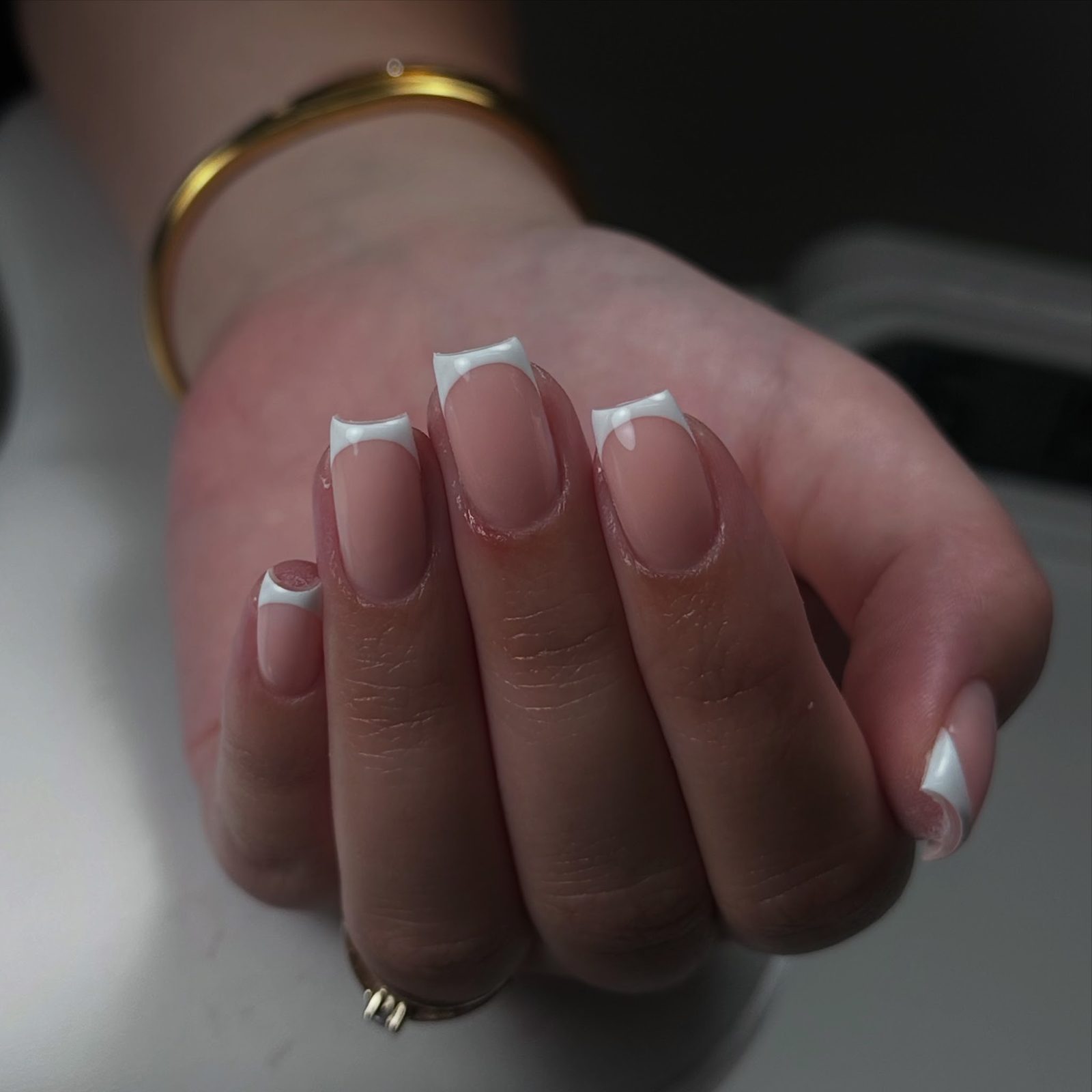 Vierkante nagels met een strakke witte French tip, close-up van een hand met een gouden armband