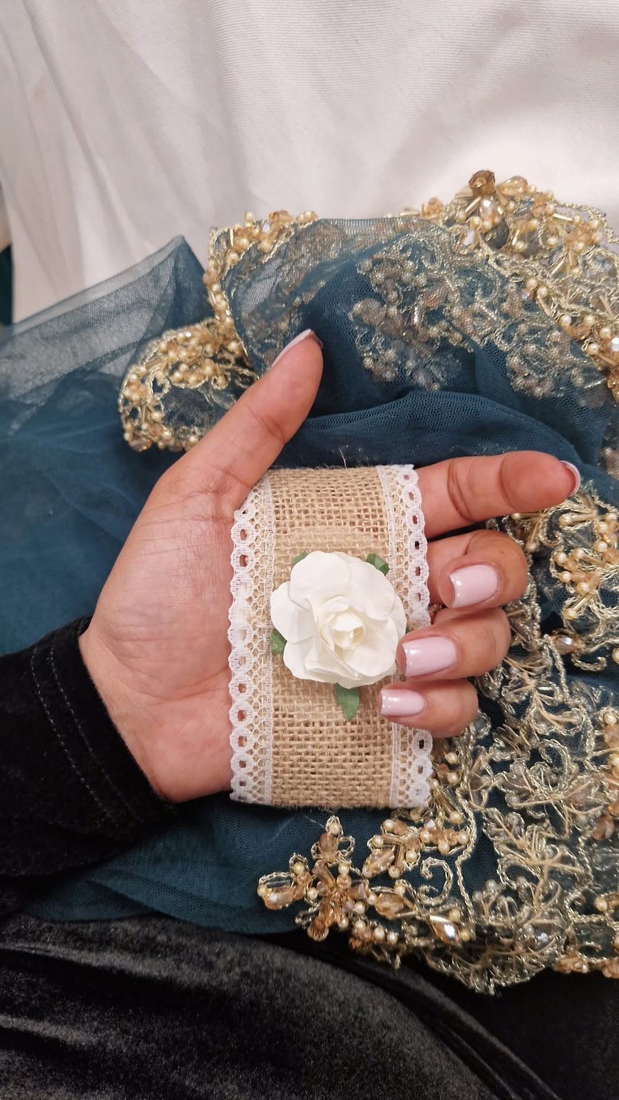 Hand met roze nagels op een kanten stof met een witte bloem