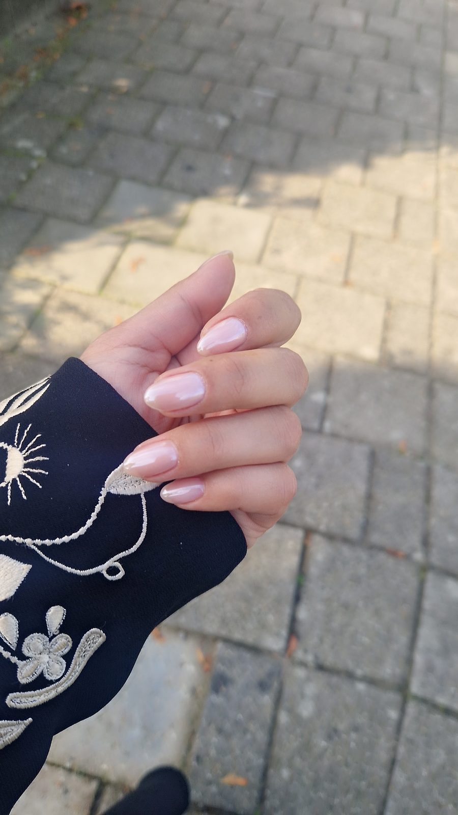 Hand met roze French nagels boven een klinkerstraat
