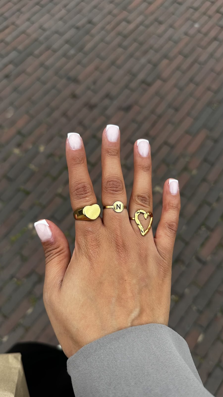 Nagels met een witte tip, ringen aan de vingers, op een klinkerstraat
