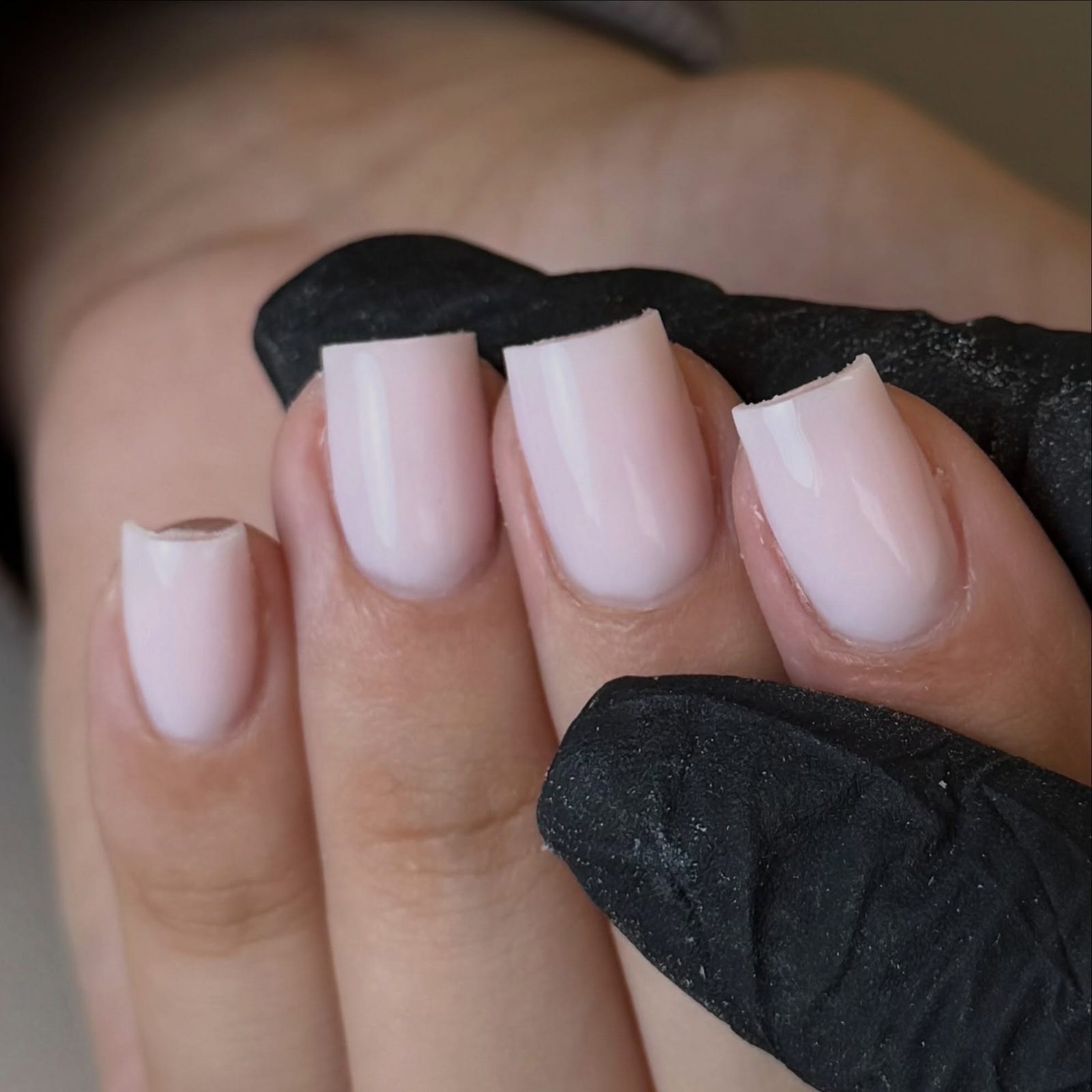 Melkwitte vierkante nagels, de hand rust op een zwarte handschoen