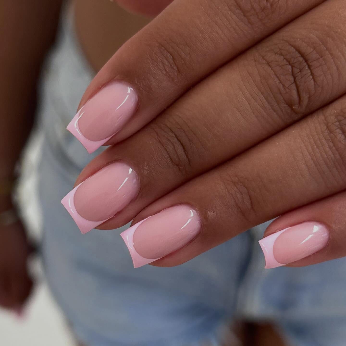 Roze nagels met een witte French tip, op de achtergrond een spijkerbroek