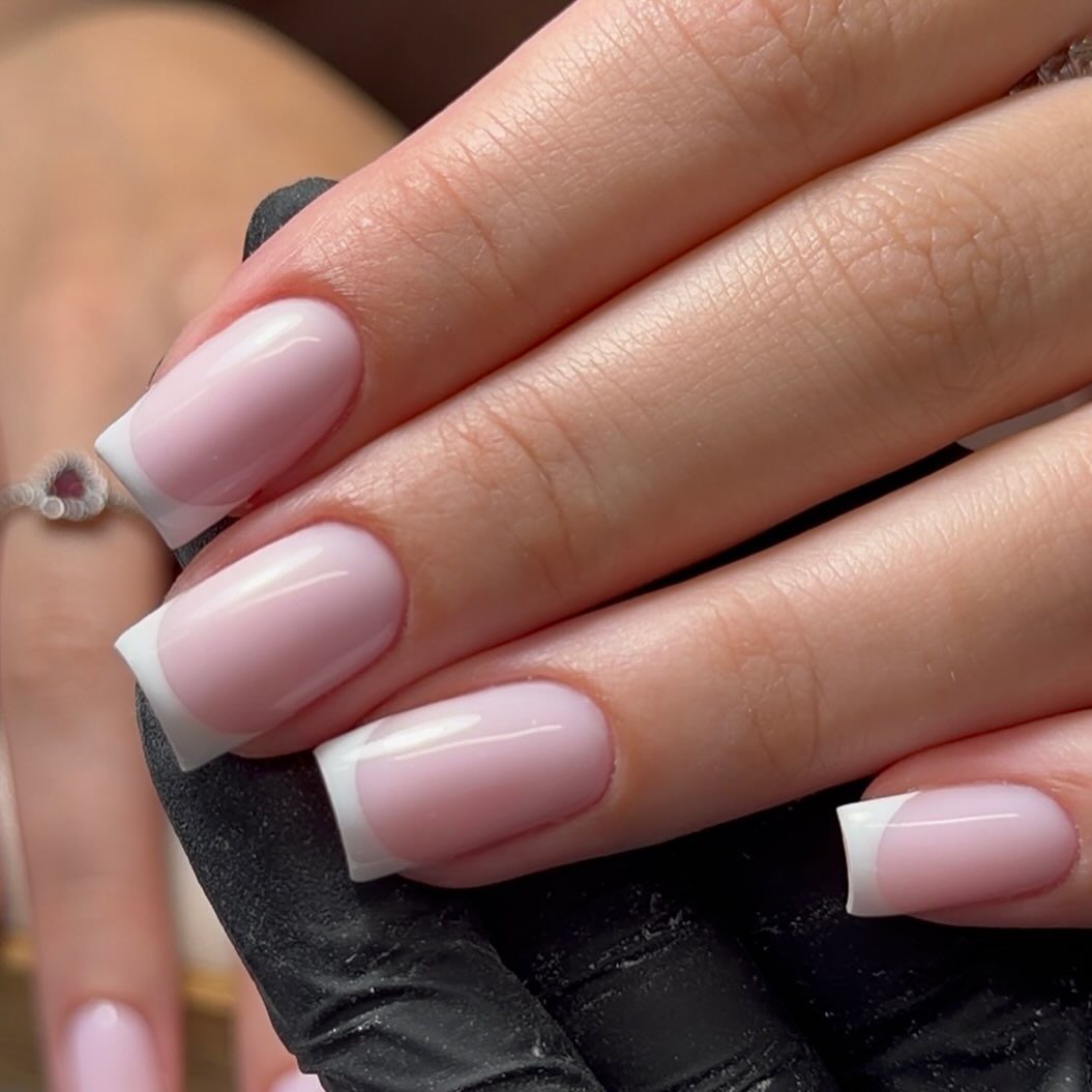 Roze nagels met een witte French tip boven een zwarte handschoen